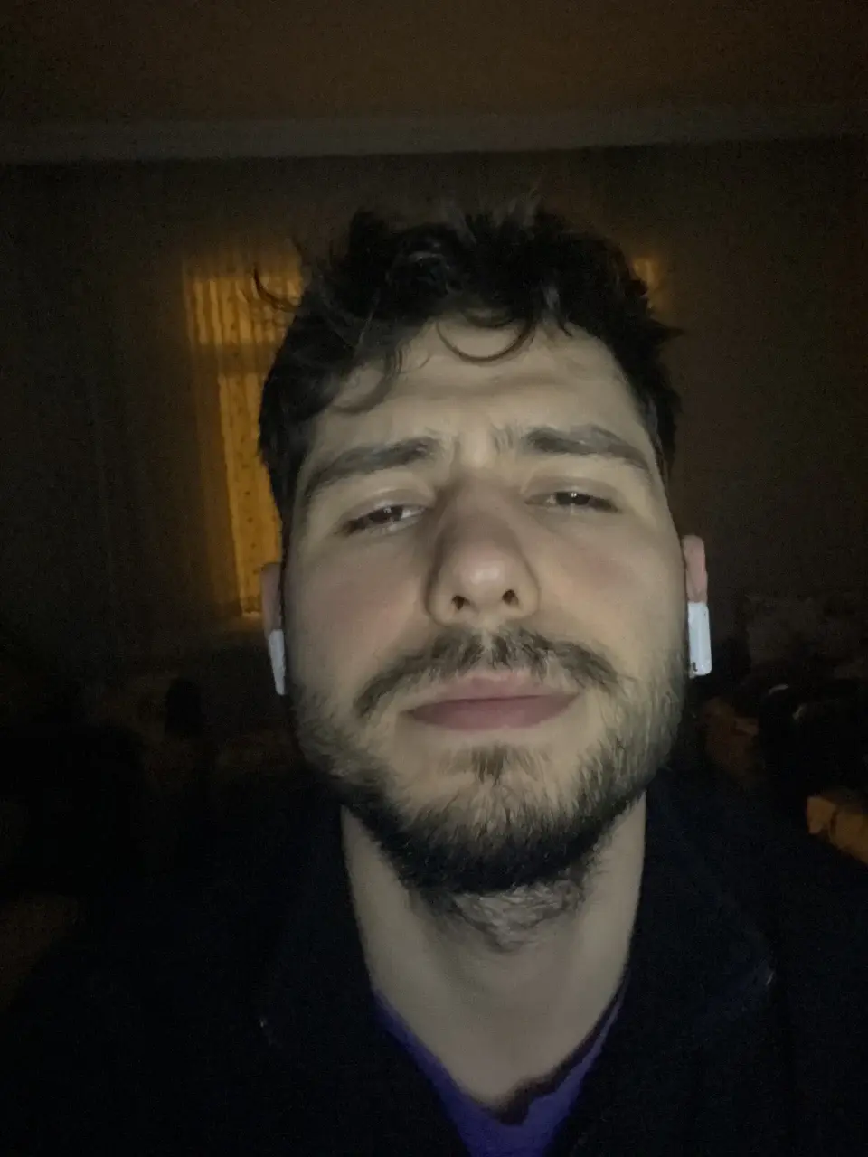 Ahmet Yasir Demir wearing wireless earphones in a dimly lit room.